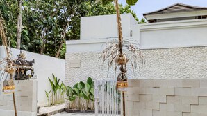 A gated entrance with a stone wall, a white gate, and a small shrine with a statue. - Belvilla Serene Haven Nusa Dua Beach (Nusa Dua)