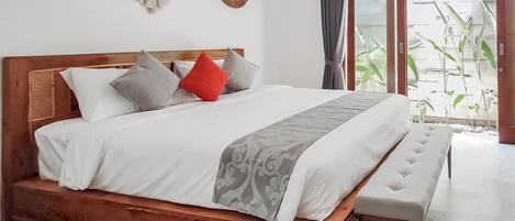 Una cama de madera con un banco, ropa de cama blanca y almohadones decorativos.