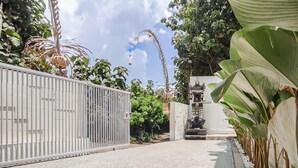 A gated pathway leading to a building with a white facade, surrounded by lush greenery and large leaves. - Belvilla Serene Haven Nusa Dua Beach (Nusa Dua)