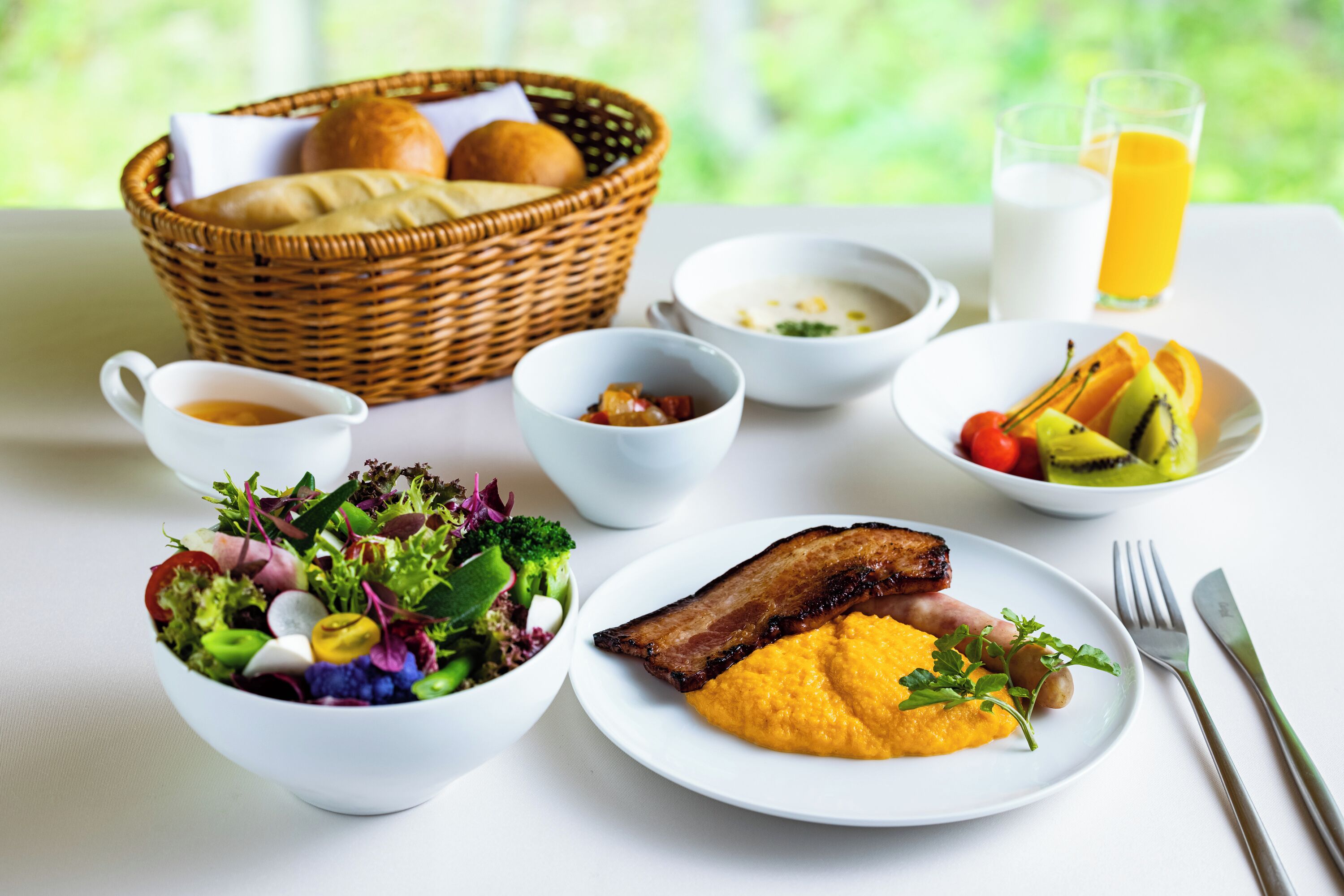 Un desayuno con una variedad de platos, como ensalada, sopa, fruta y carne.