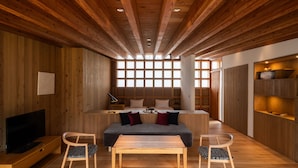 Un intérieur moderne avec des murs en bois, un canapé, deux fauteuils, une table, un téléviseur et une grande fenêtre laissant entrer la lumière naturelle.