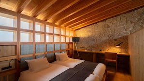 Une chambre avec un grand lit, un bureau et un mur en pierre.