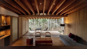 Un intérieur moderne avec un plafond en bois, un canapé, une table et des chaises. On peut admirer une forêt à travers une porte vitrée.