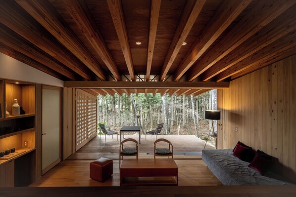 Un interior moderno con techo de madera, un sofá, una mesa y sillas. Se ve un bosque a través de una puerta de cristal.