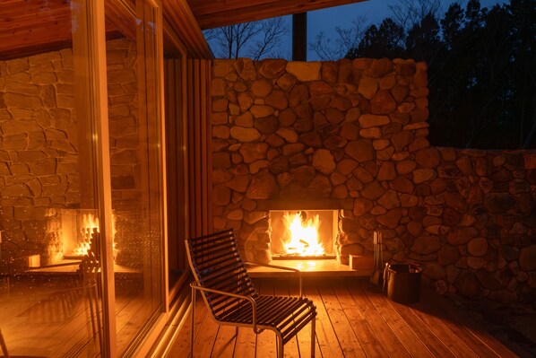 Ein Steinkamin mit Feuer, eine Holzterrasse und eine Glastür zu einem Raum.