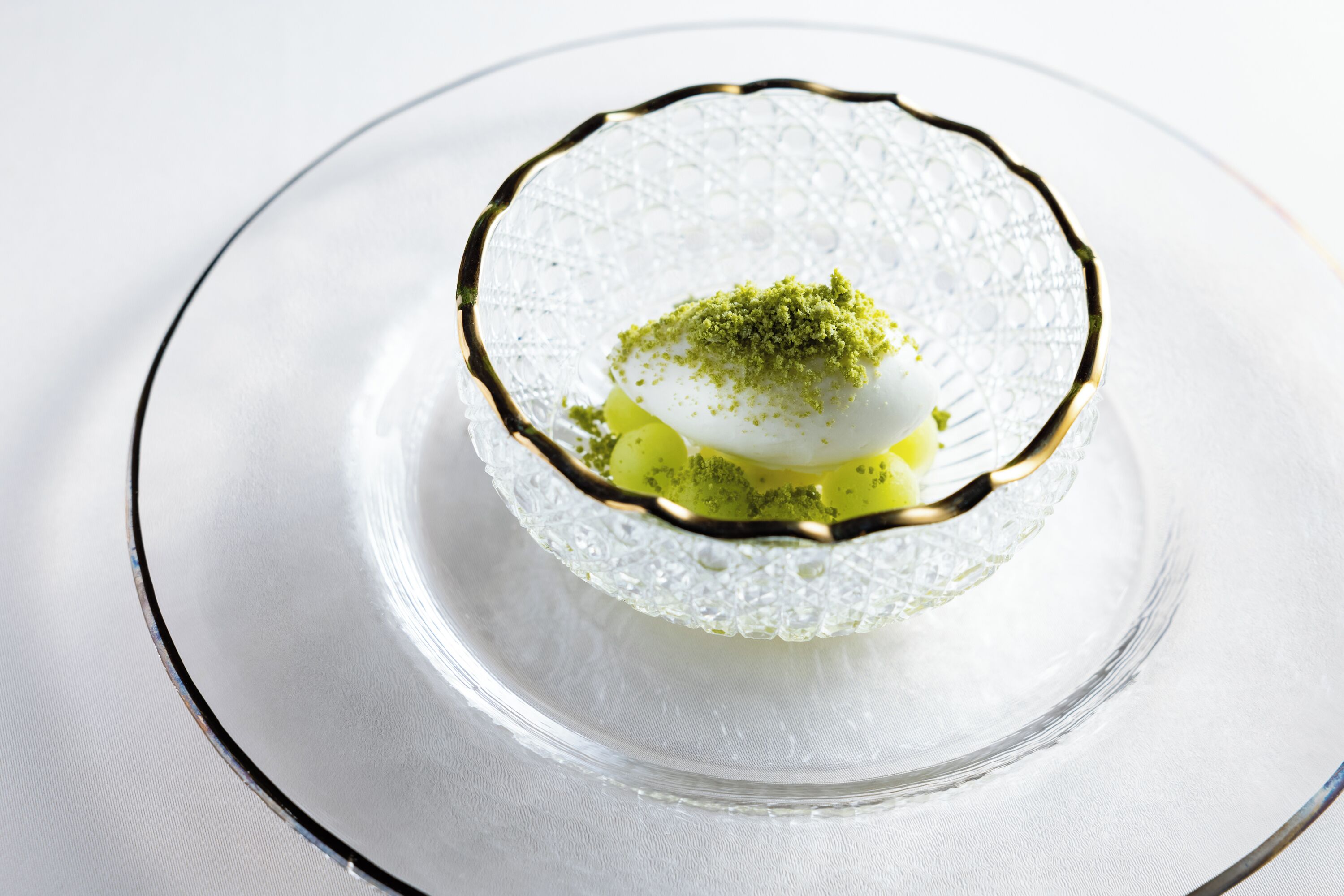 A clear glass dessert dish with a gold rim on a white tablecloth.