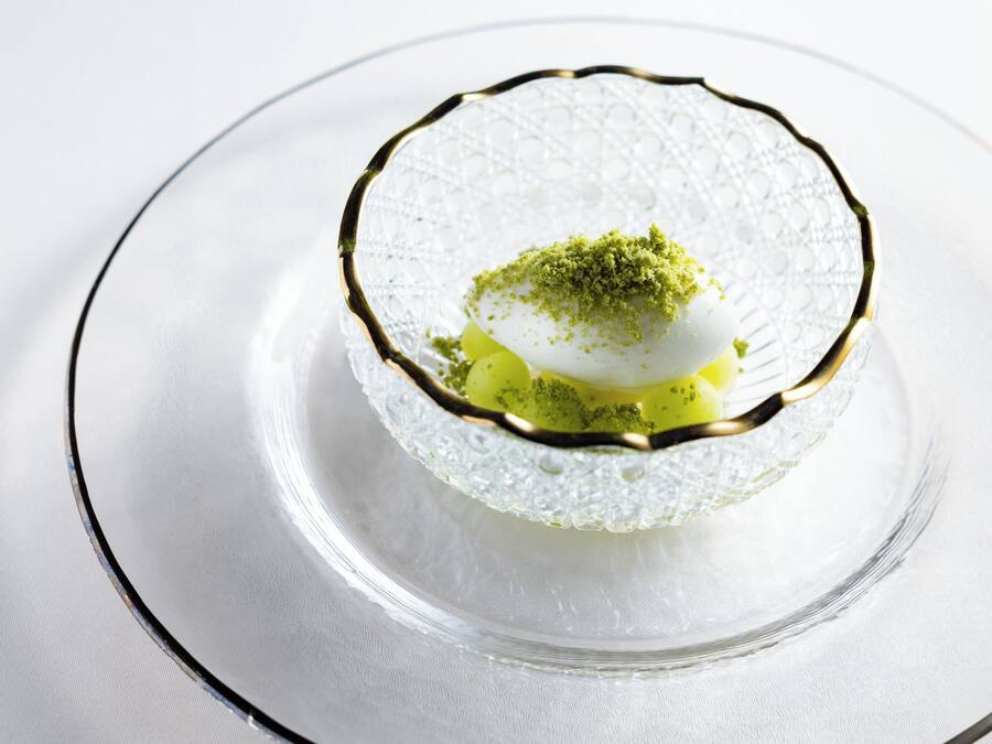A clear glass dessert dish with a gold rim on a white tablecloth.