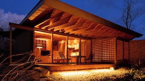 Une maison moderne avec une façade en bois, un porche couvert et un intérieur visible comprenant un coin repas.