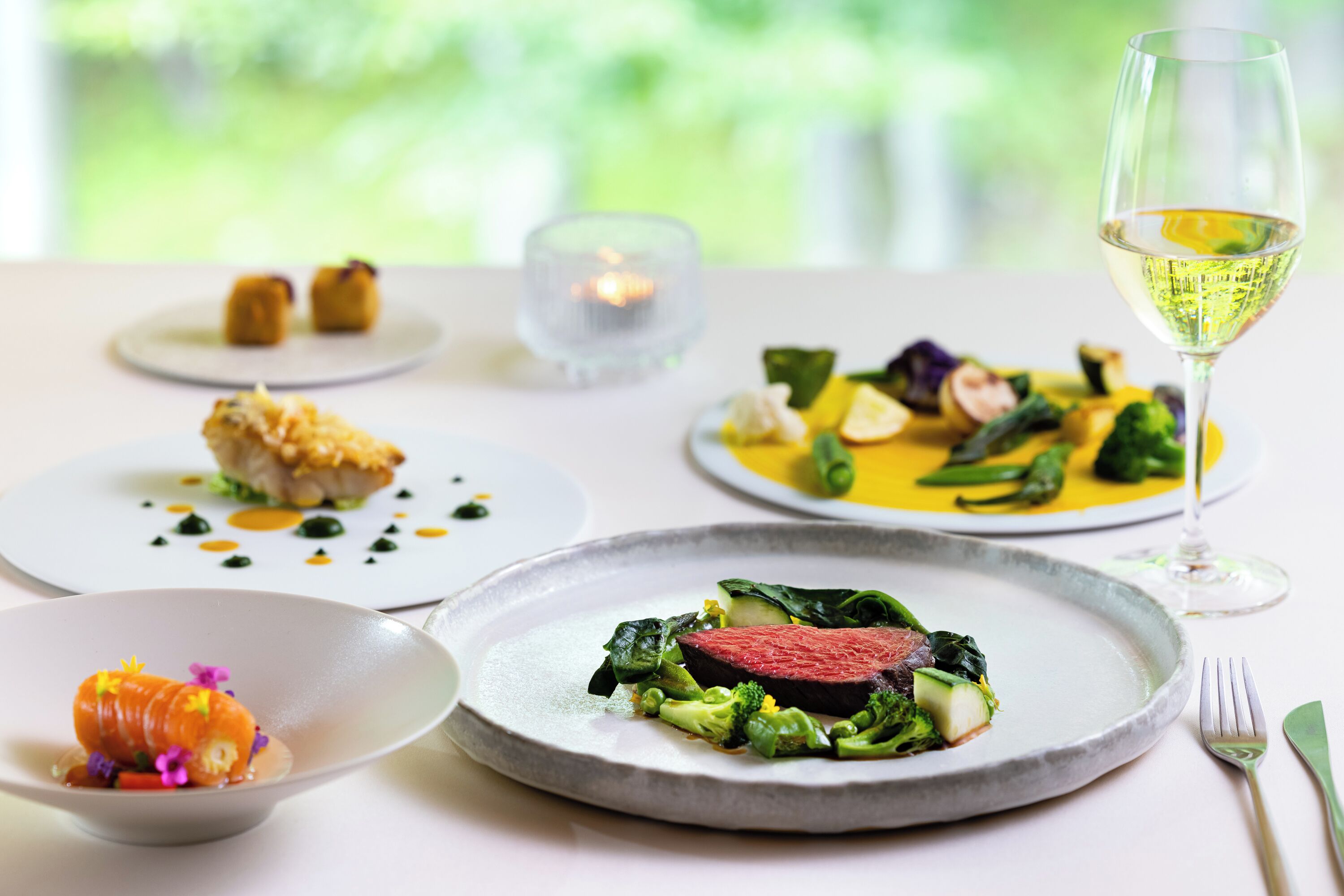 A dining table with various dishes and a glass of white wine.