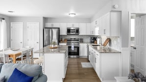 A modern kitchen with white cabinetry, a central island, stainless steel appliances, and a dining area with a table and chairs.