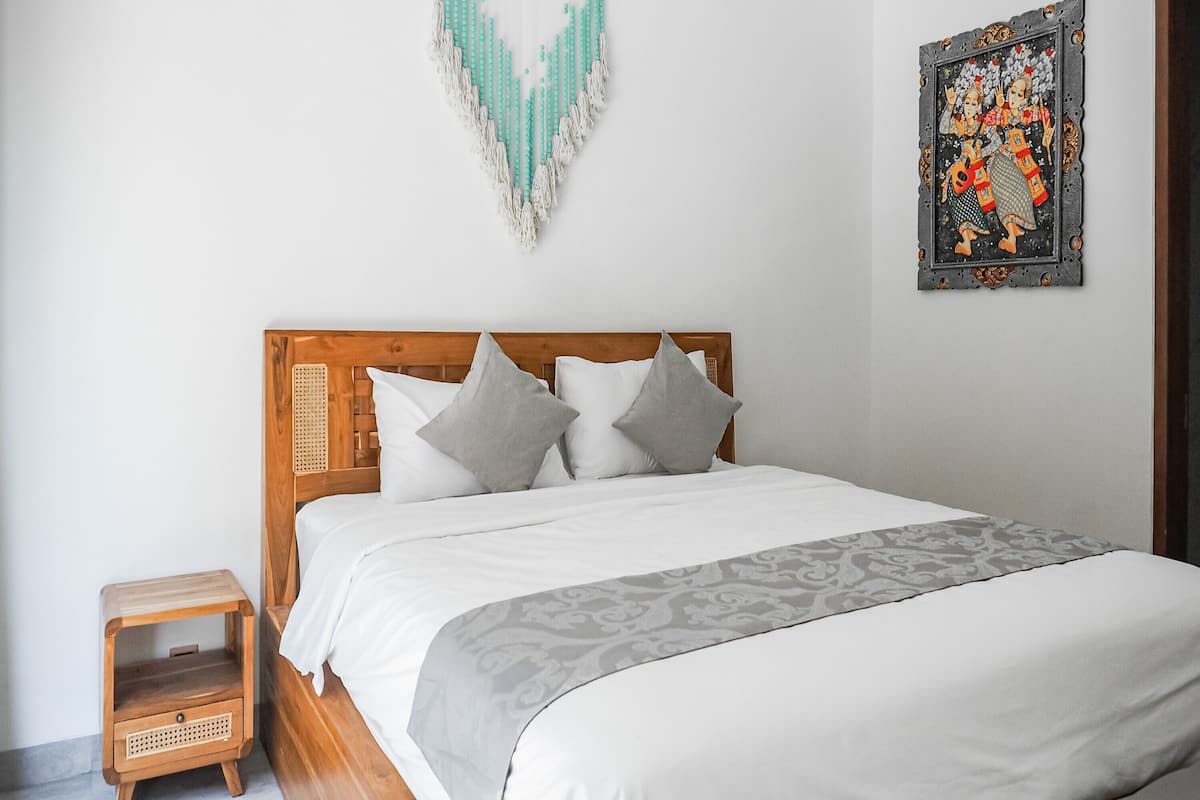 A neatly made bed with a wooden headboard, a small wooden nightstand, and a decorative wall hanging.