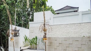 A gated entrance with a white wall and a stone wall, a white gate, and a scooter parked nearby. - Belvilla Calm Woods Pandawa Beach (Nusa Dua)