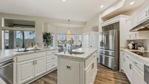 A spacious kitchen with white cabinetry, a large island, stainless steel appliances, and a view of a pool and palm trees. - 5BR w lake view, heated pool, hot tub, sauna (Gilbert)