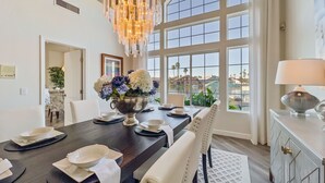 A dining area with a dark wooden table, white chairs, a chandelier, and a view of a water body through large windows. - 5BR w lake view, heated pool, hot tub, sauna (Gilbert)