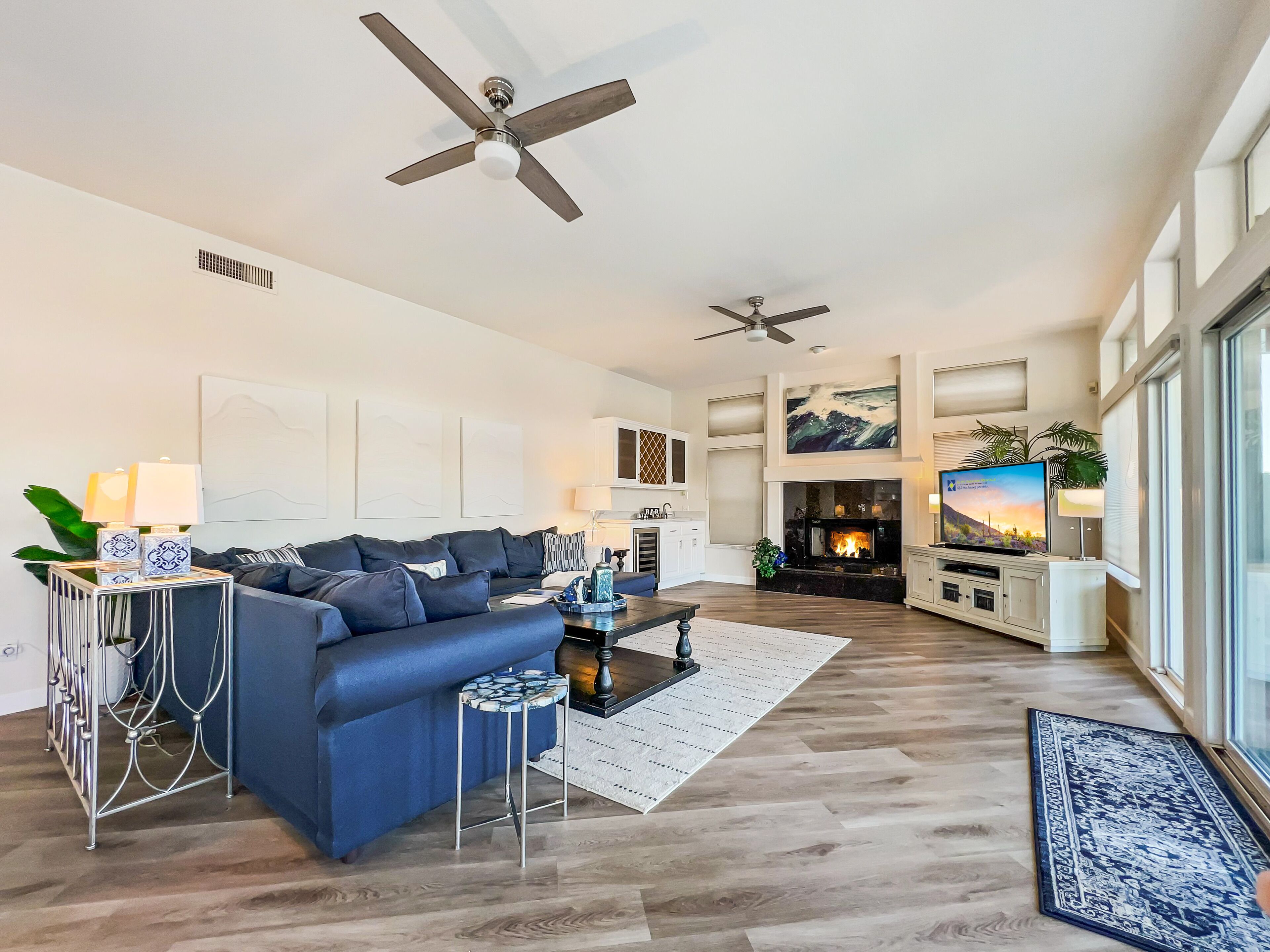 A spacious living room with a dark blue sofa, a fireplace, a television, and two ceiling fans.