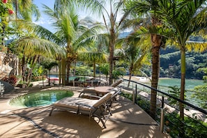 Zona junto a la piscina con sillas de descanso, un jacuzzi y vistas a un río y montañas.