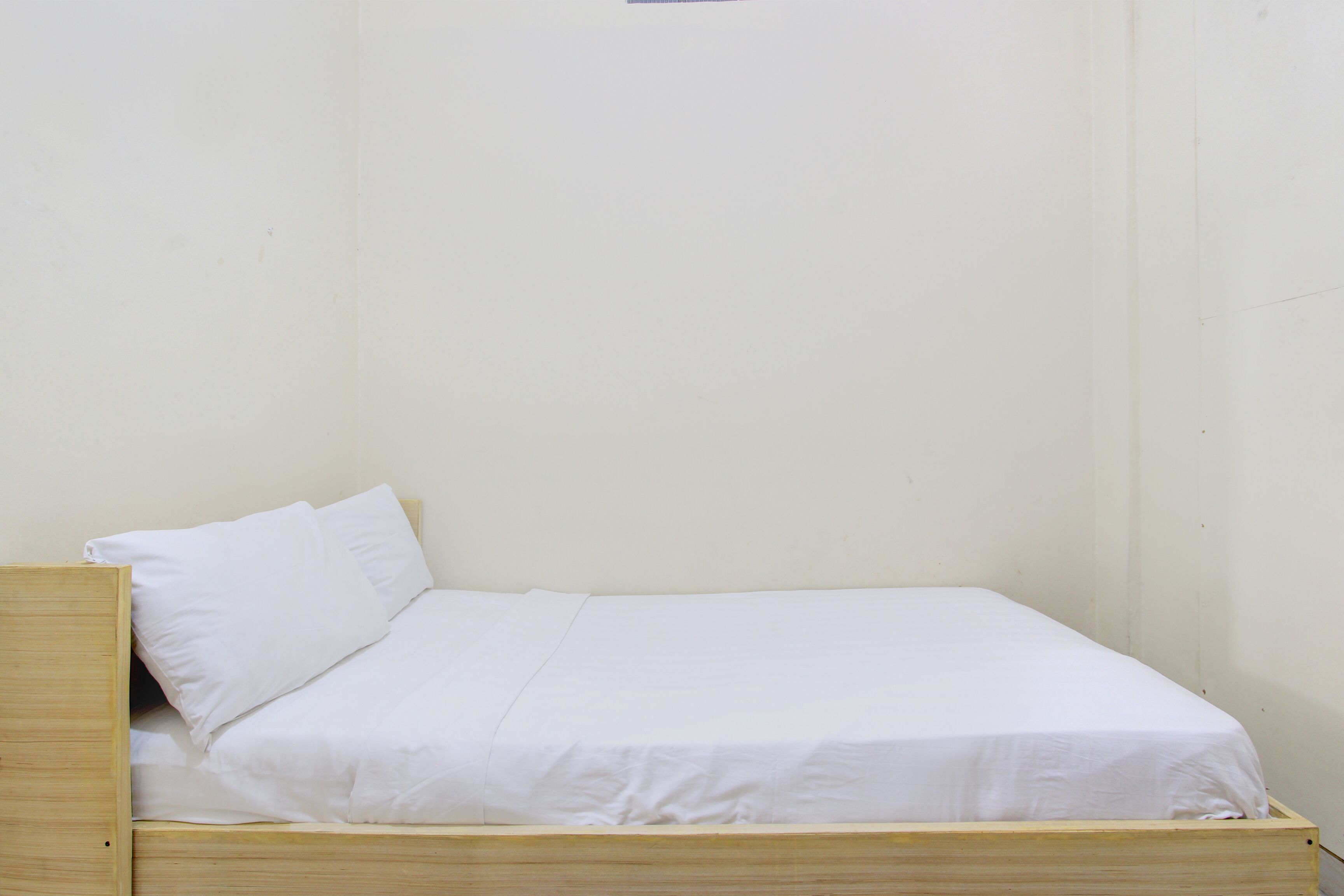 Un lit simple avec une literie blanche, dans une pièce aux murs blancs et unis.