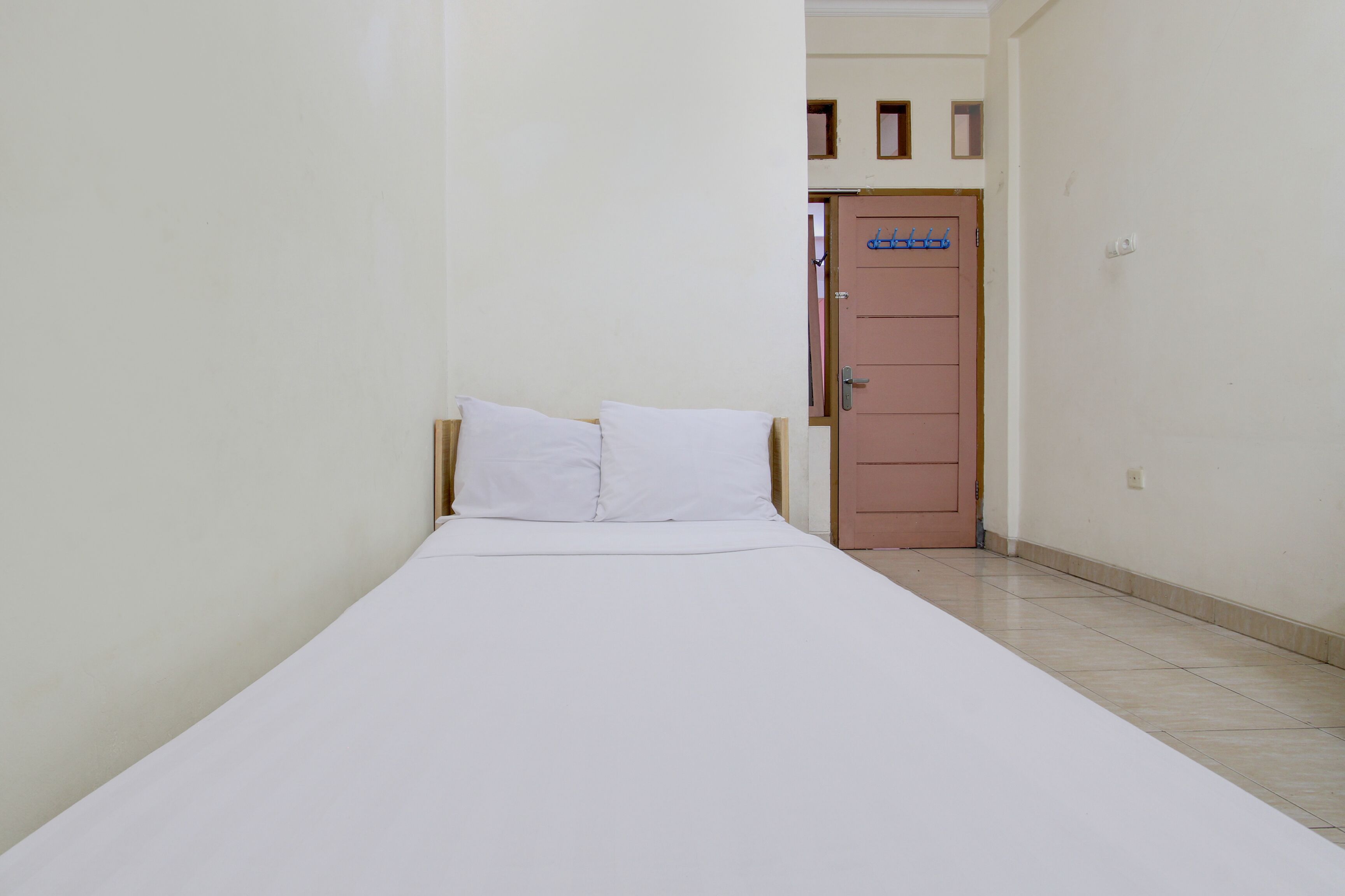 A small, narrow room with a single bed, a door, and a tiled floor.