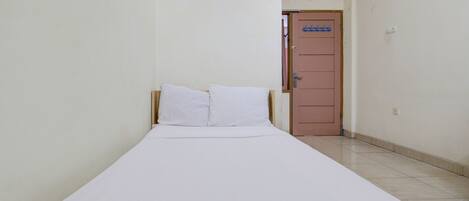 Una habitación pequeña y estrecha con una cama individual, una puerta y piso de baldosas.