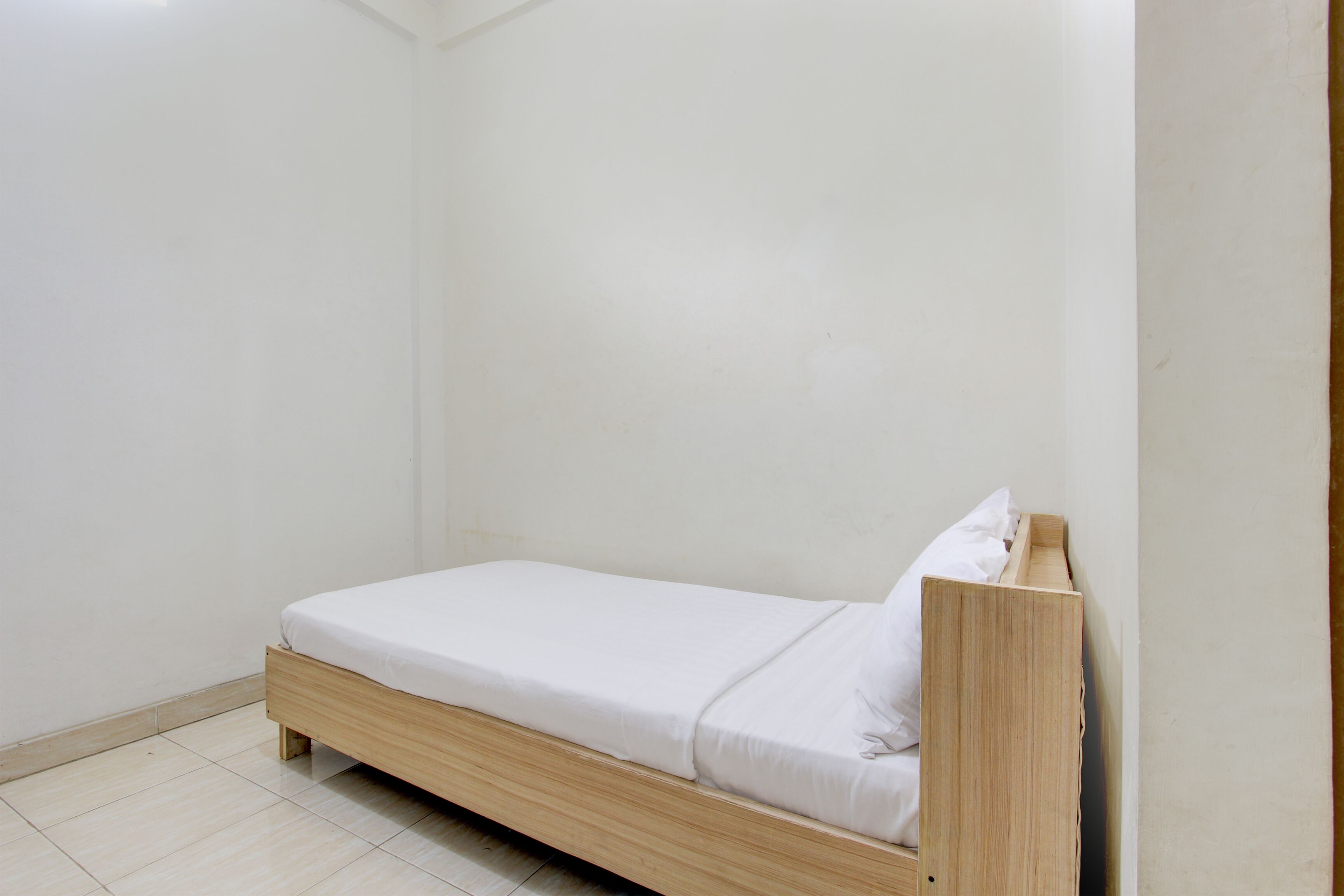Ein kleines Zimmer mit einem Einzelbett, einem Holzrahmen und weißer Bettwäsche.