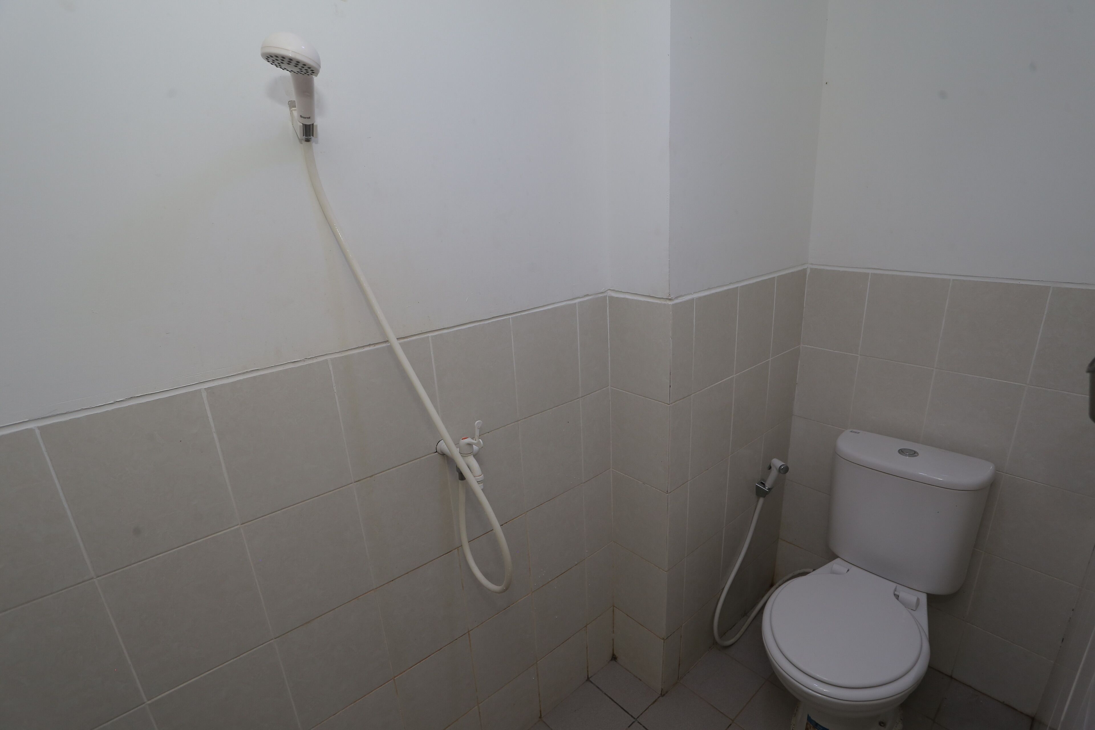 A small bathroom with a toilet, a shower head, and a handheld shower attachment.
