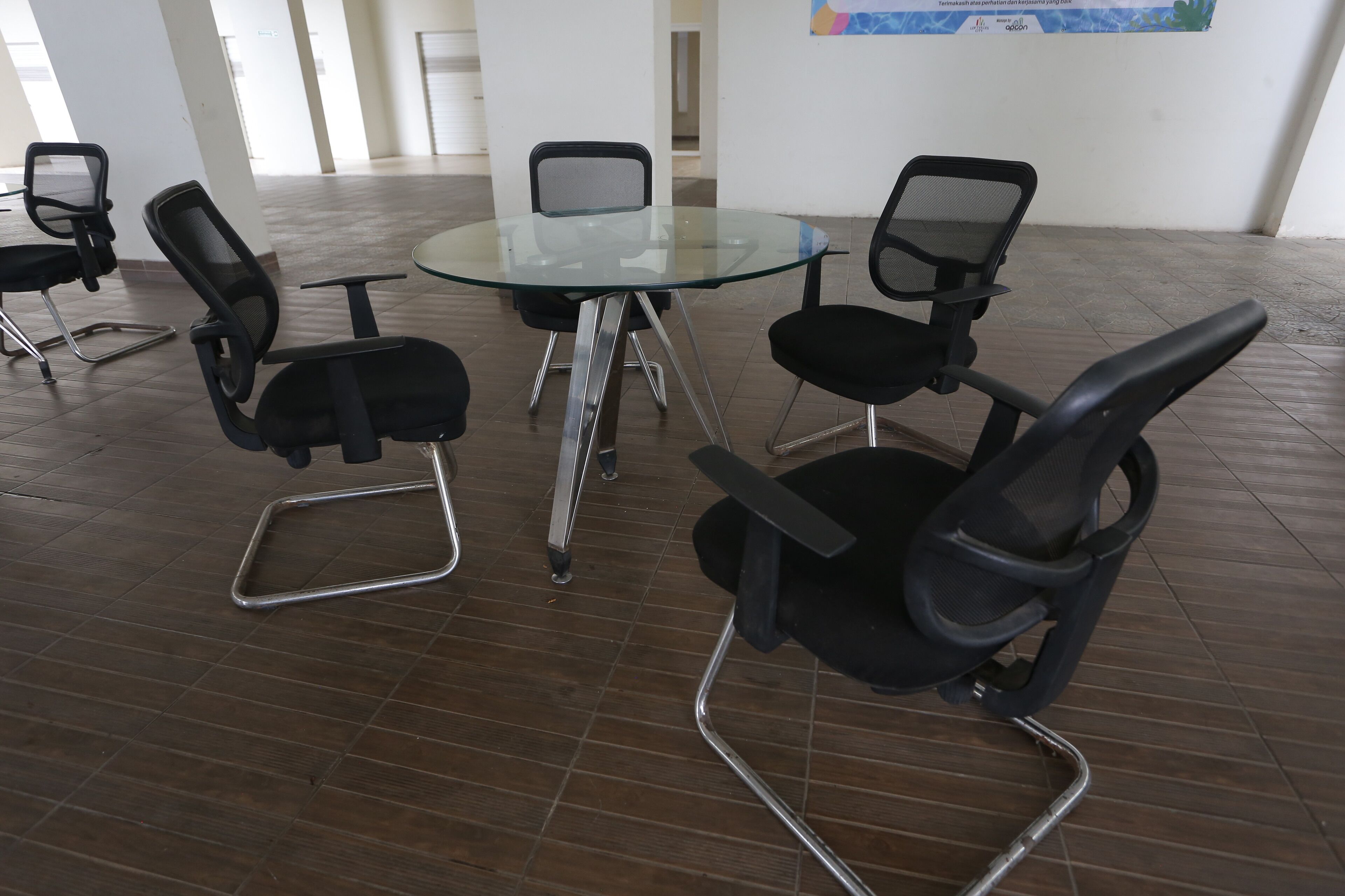 Un salón de conferencias con una mesa de vidrio rodeada por cuatro sillas de oficina negras con estructura metálica.