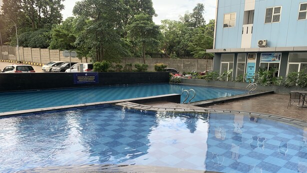 Ein Schwimmbecken mit Schachbrettmuster, umgeben von einer Holzterrasse und einer Betonmauer.
