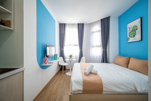 A hotel room with a bed, a desk, a chair, a small table with a plant, and a window with curtains. - Cozrum Homes - Selina Residence (Ho Chi Minh City)