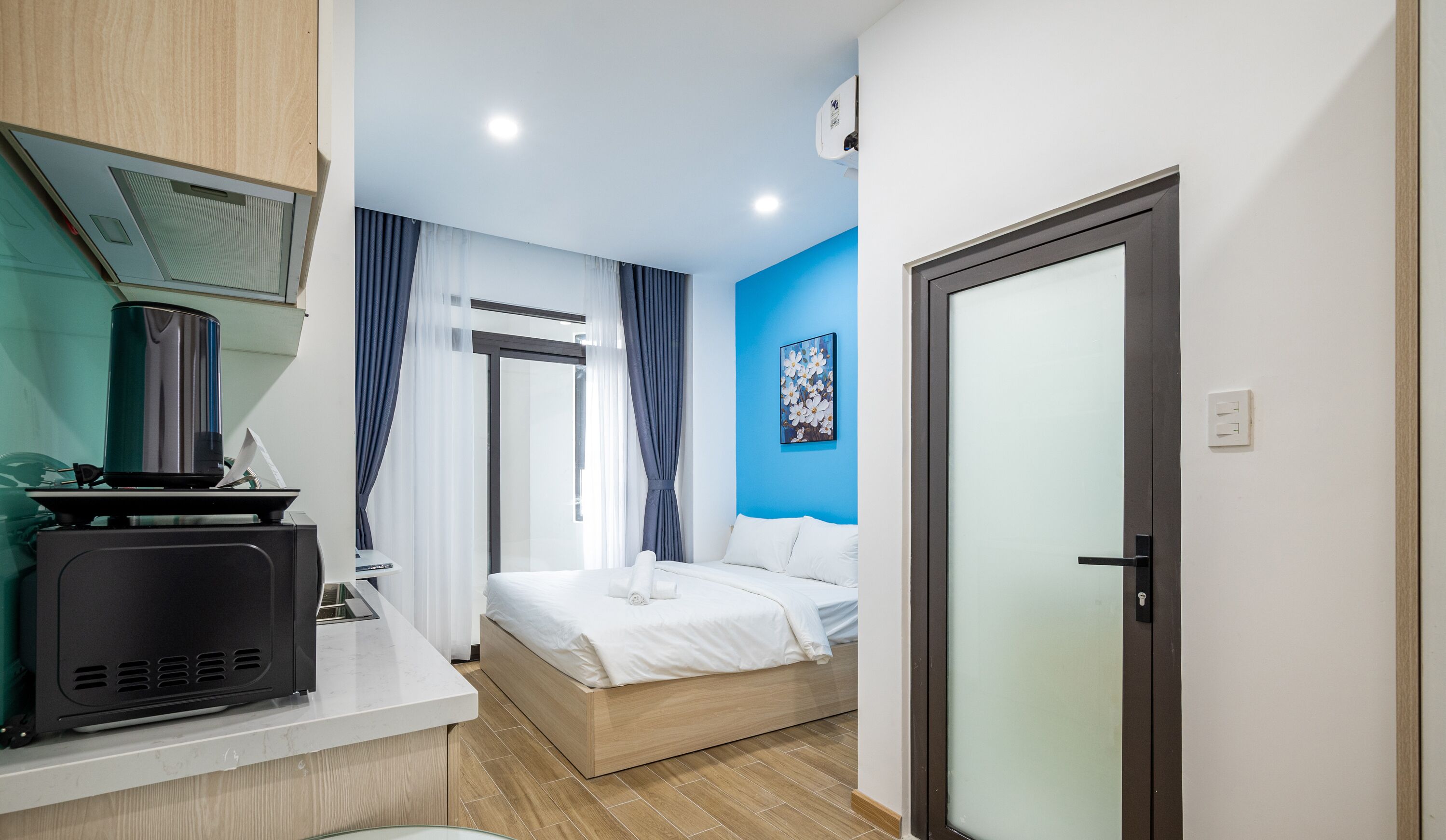 A modern hotel room with a bed, a desk with a kettle, and a shower area.