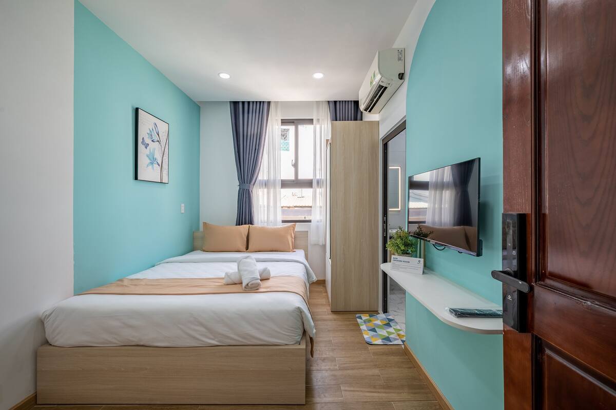 A modern hotel room with two beds, a TV, and a small desk area.