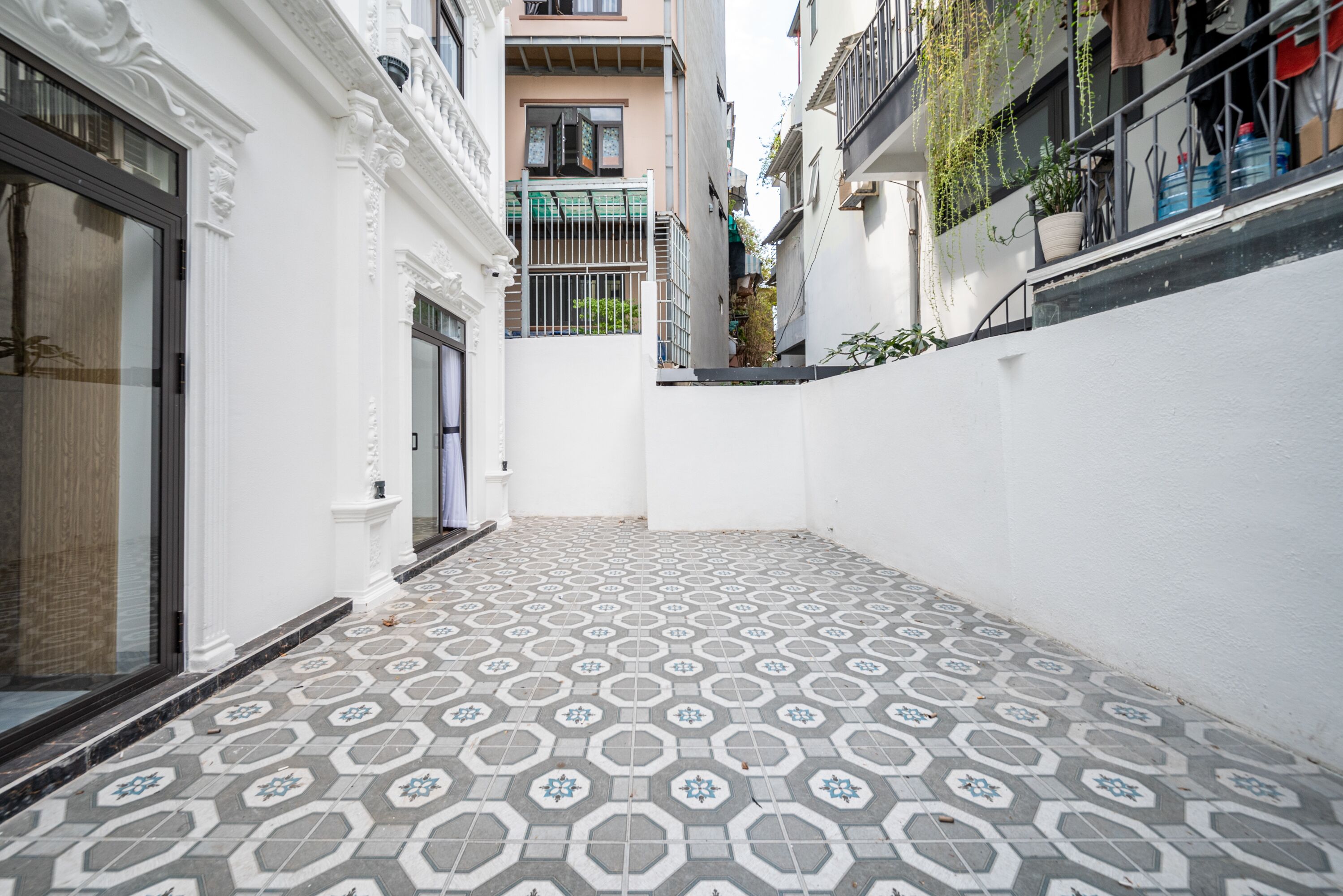 A narrow alleyway with patterned tile flooring, white walls, and a metal gate.