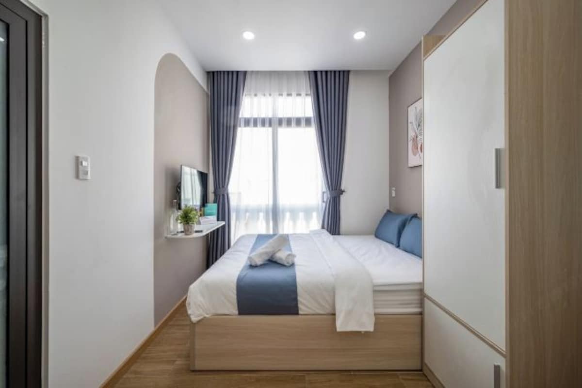 Une chambre à coucher moderne avec un lit, une table de chevet, un miroir et une fenêtre avec des rideaux.