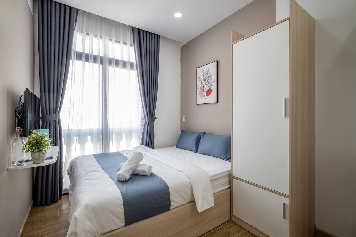 A modern hotel room with a neatly made bed, a bedside table with a plant, and a large wardrobe.
