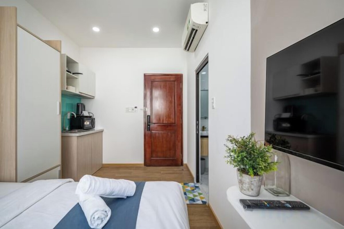 Habitación de hotel con cama, escritorio con computadora, televisor y una pequeña kitchenette.
