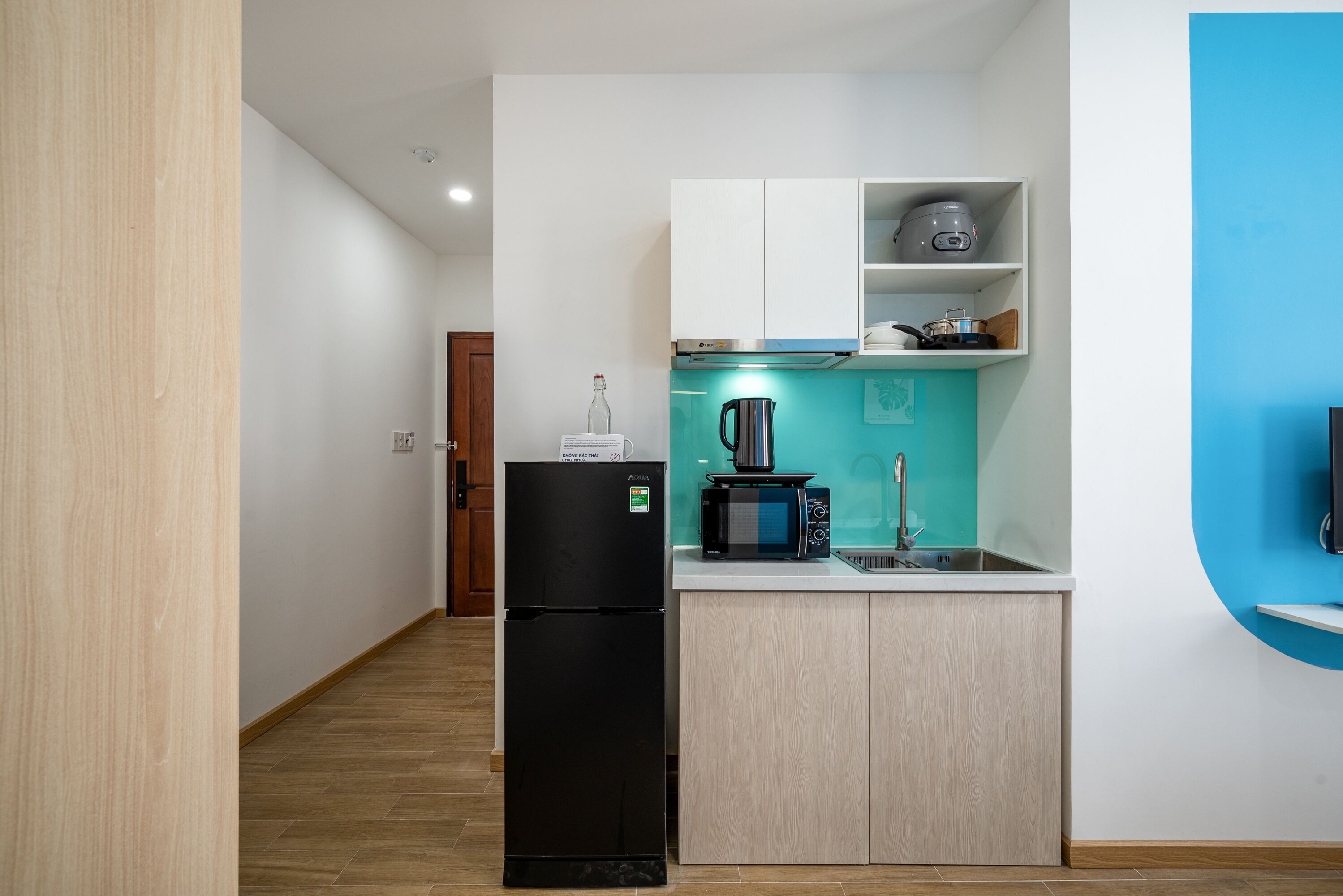 Eine kleine Küche mit einem schwarzen Kühlschrank, einer Mikrowelle, einem Wasserkocher und einem Spülbecken.