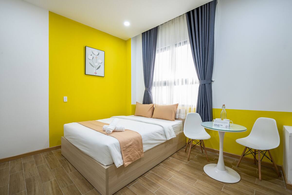 A room with a bed, a small round table, two chairs, and a window with curtains.