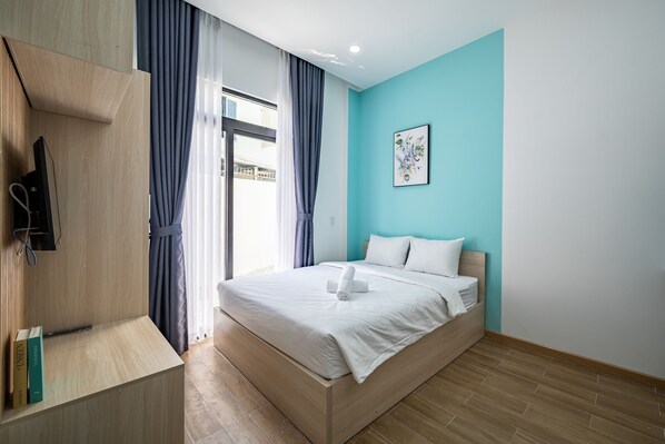 A modern bedroom with a wooden bed, a TV mounted on the wall, and a window with curtains. - Cozrum Homes - Selina Residence (Ho Chi Minh City)