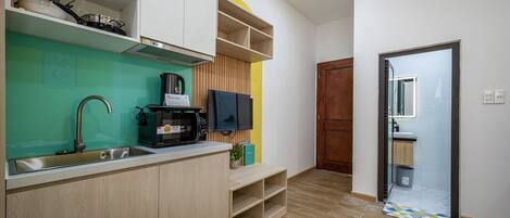 A compact kitchen with a sink, microwave, and a flat-screen TV.