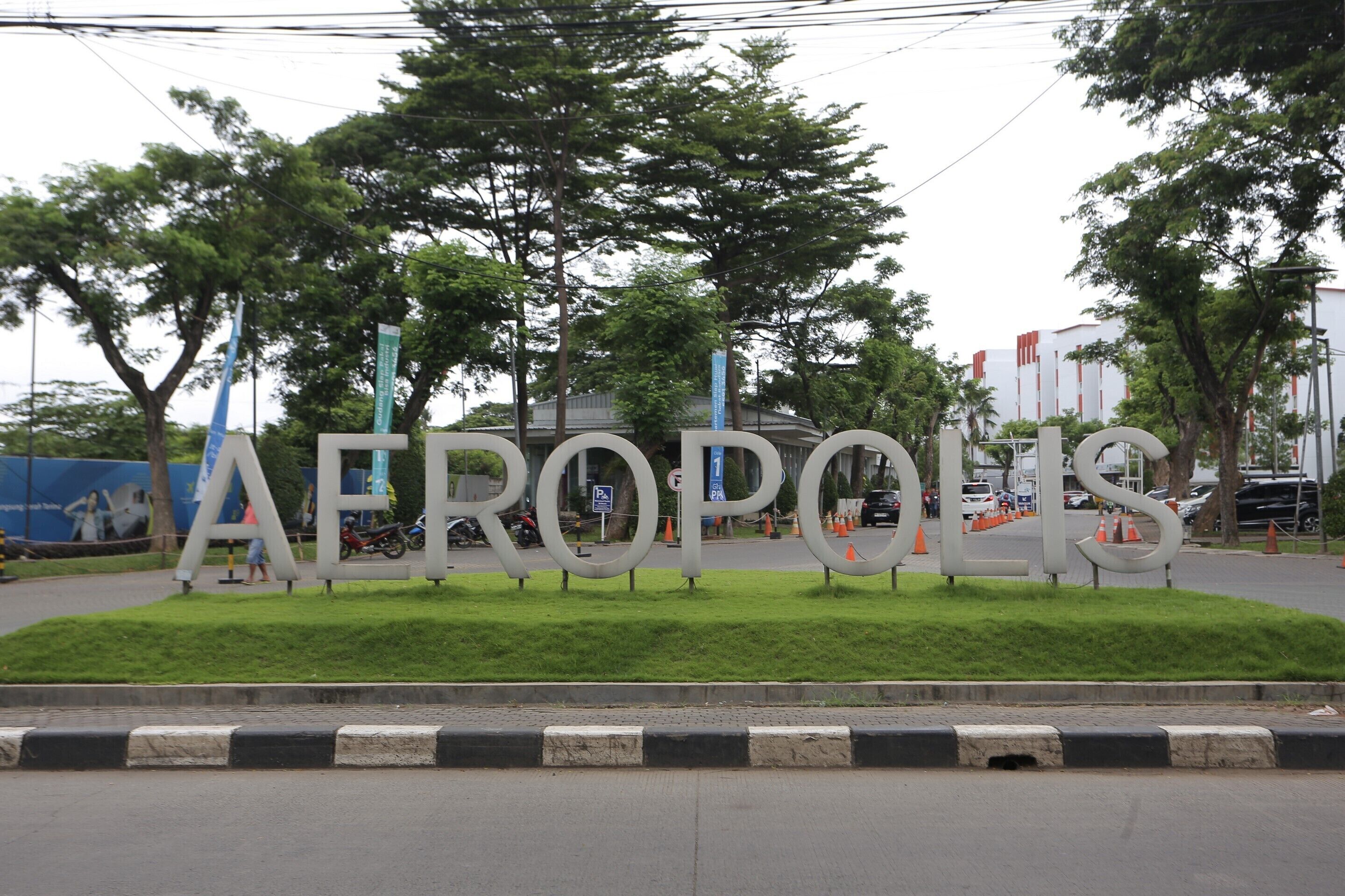 A large sign with the word "AEROPOLIS" in the foreground, surrounded by greenery and trees.