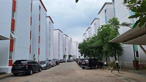A parking area with multiple cars parked in rows, surrounded by modern buildings with red accents and large windows. - Hotel O Room Transit By At (Tangerang)