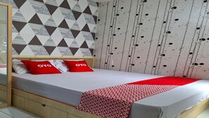 A neatly made bed with a patterned blanket and red pillows, a wooden headboard, and a wall with geometric and circular patterns. - Hotel O Room Transit By At (Tangerang)