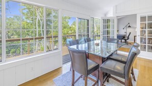 A spacious dining area with a glass table and chairs, large windows with a view of greenery, and a ceiling fan. - Gertrude's Siesta | Pool & Spa, 100% Private, 5-min bike to Siesta Key Beach, 3-miles to Village! (Siesta Key)