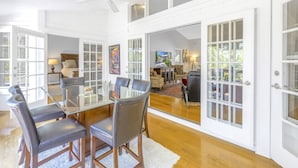 A spacious dining area with a glass-top table and leather chairs, white paneled walls, and a view of an outdoor patio through large French doors. - Gertrude's Siesta | Pool & Spa, 100% Private, 5-min bike to Siesta Key Beach, 3-miles to Village! (Siesta Key)