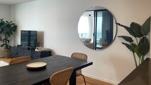 Un espace repas moderne avec une table en bois foncé, des chaises en osier et un grand miroir au mur.