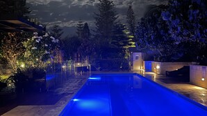 Une piscine éclairée de lumières bleues, entourée d’arbres et bordée d’un bâtiment dont les fenêtres sont illuminées.