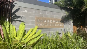 Une enseigne indiquant la promenade de Burleigh Beach, avec un mur de pierres et une végétation luxuriante au premier plan.