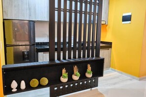 A modern kitchen with a black countertop, a stainless steel refrigerator, and a yellow accent wall.