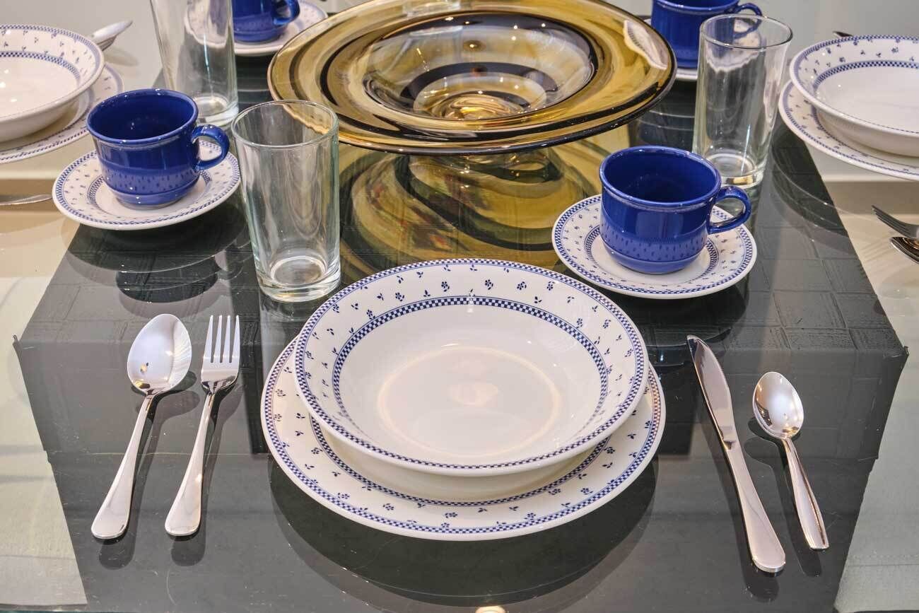 A dining table set with blue and white plates, silverware, and blue cups.