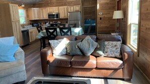 A cozy cabin interior with a brown leather sofa, a grey armchair, and a dining area with a table and chairs. - Lakeside House & Cabin Boat Ramp, Dock, & Fire Pit on Possum Kingdom Lake (Graham)