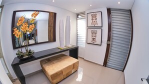 Un intérieur moderne avec une console noire, un banc beige, un grand miroir et des œuvres d’art encadrées accrochées aux murs.